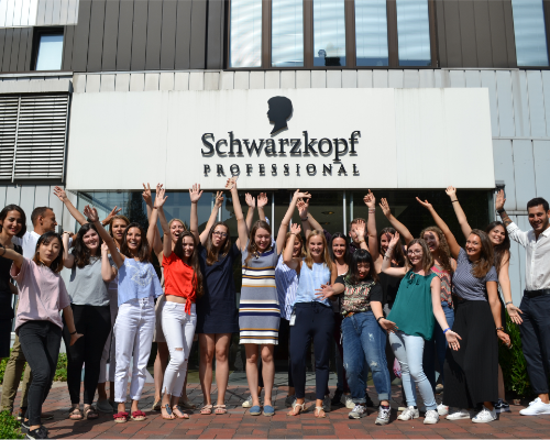 Een diverse Henkel team staat voor het Schwarzkopf professional gebouw te juichen en ze steken hun armen op. 