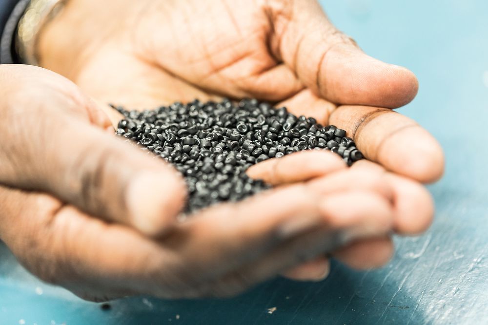 Two hands holding several black terracycle pellets