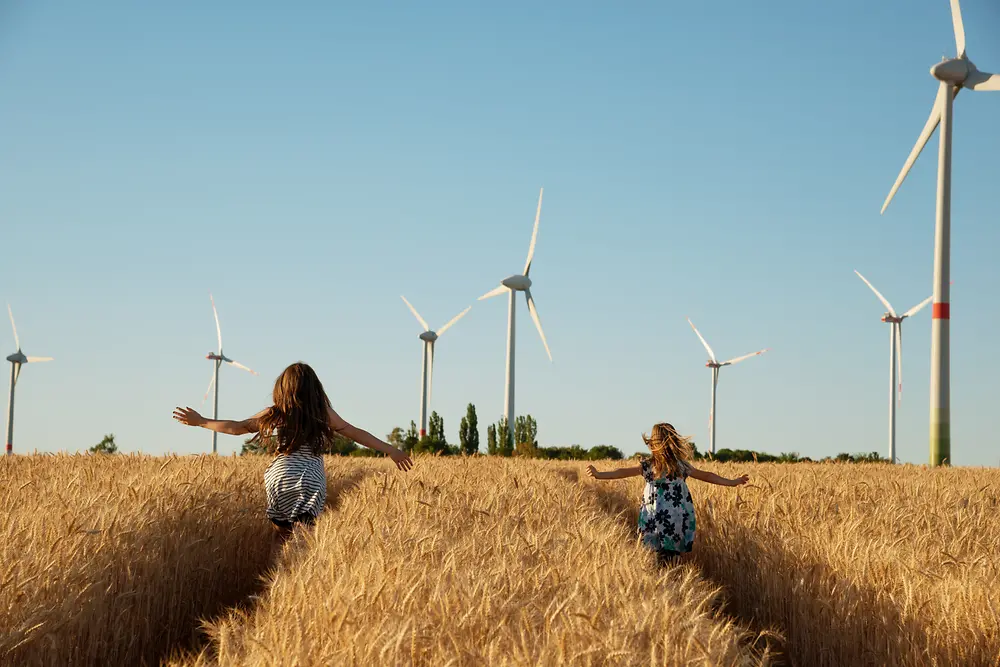 Des filles courent dans un champ en direction d'éoliennes.