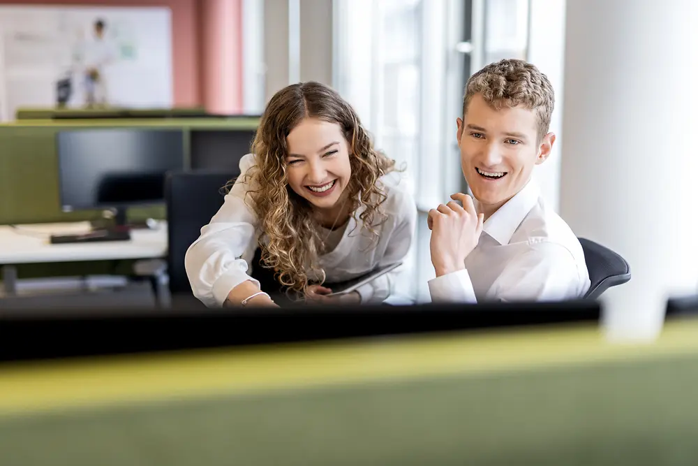 Deux jeunes professionnels collaborent à un bureau dans un environnement de bureau moderne, représentant des emplois étudiants et des postes de débutant.