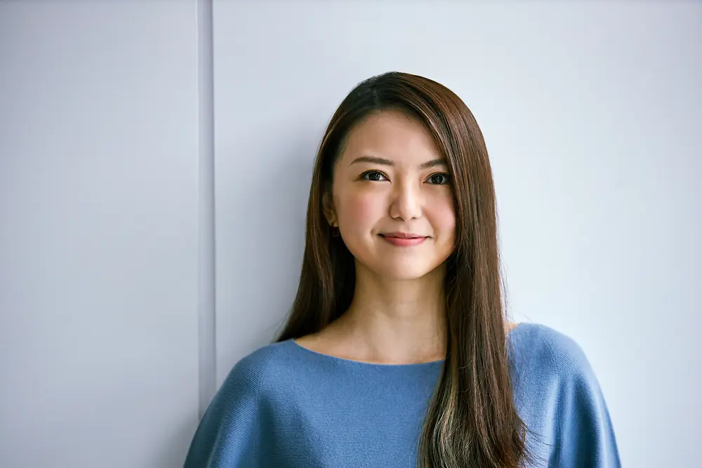 Employé en milieu de carrière debout contre un mur de couleur claire, vêtu d'un haut bleu. L'image véhicule le professionnalisme et l'expérience, et convient pour illustrer l'évolution de carrière et les opportunités chez Henkel.