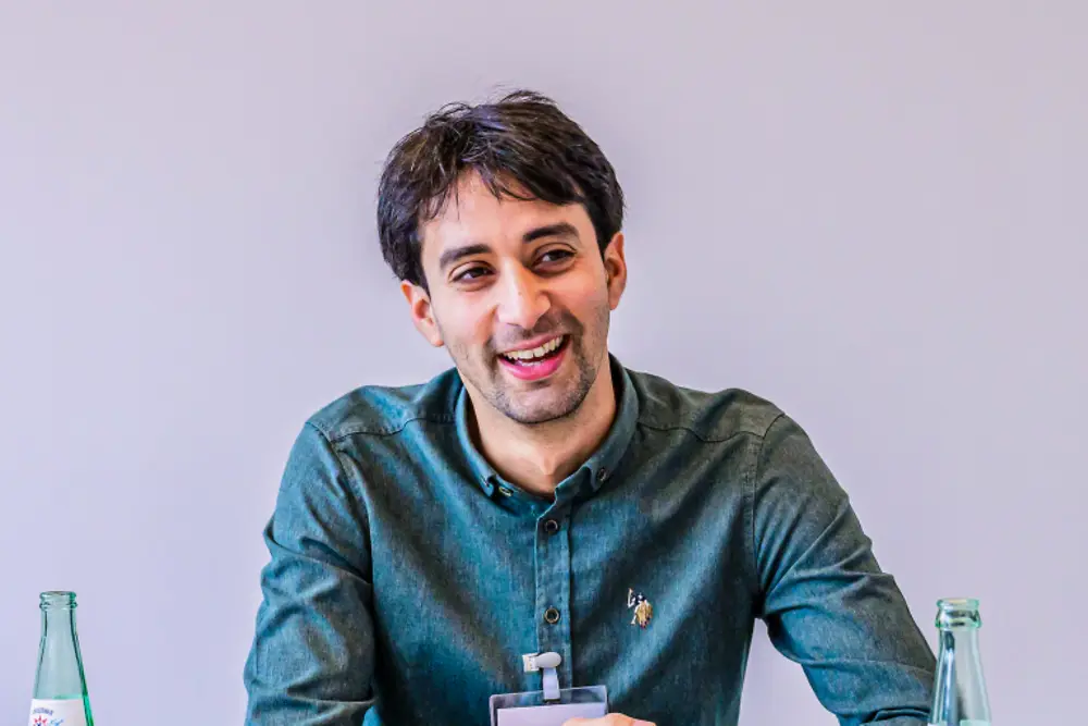 Un cadre supérieur dans un cadre de réunion professionnelle, assis de l'autre côté d'une table avec des documents lors d'une session stratégique chez Henkel.