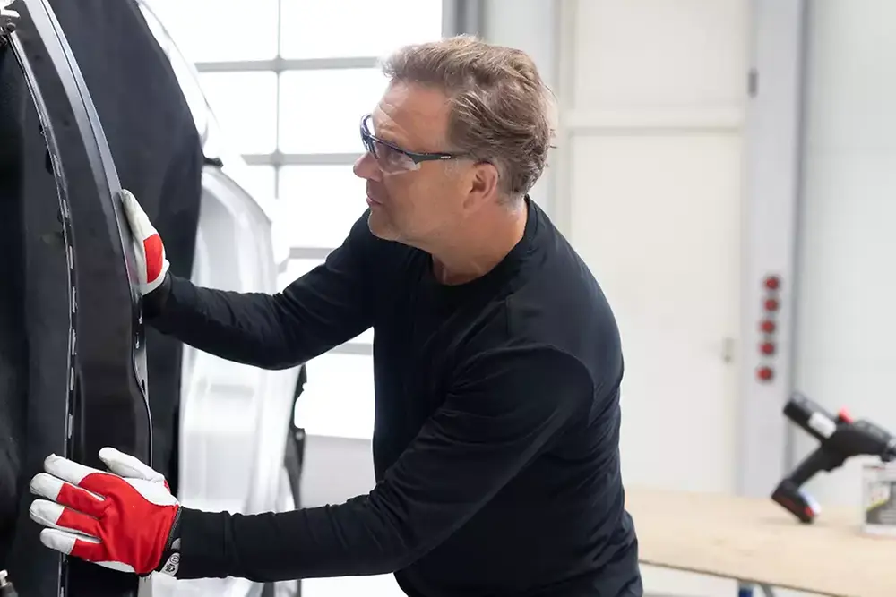 Technicien réparant ou entretenant une portière de véhicule dans un atelier automobile.